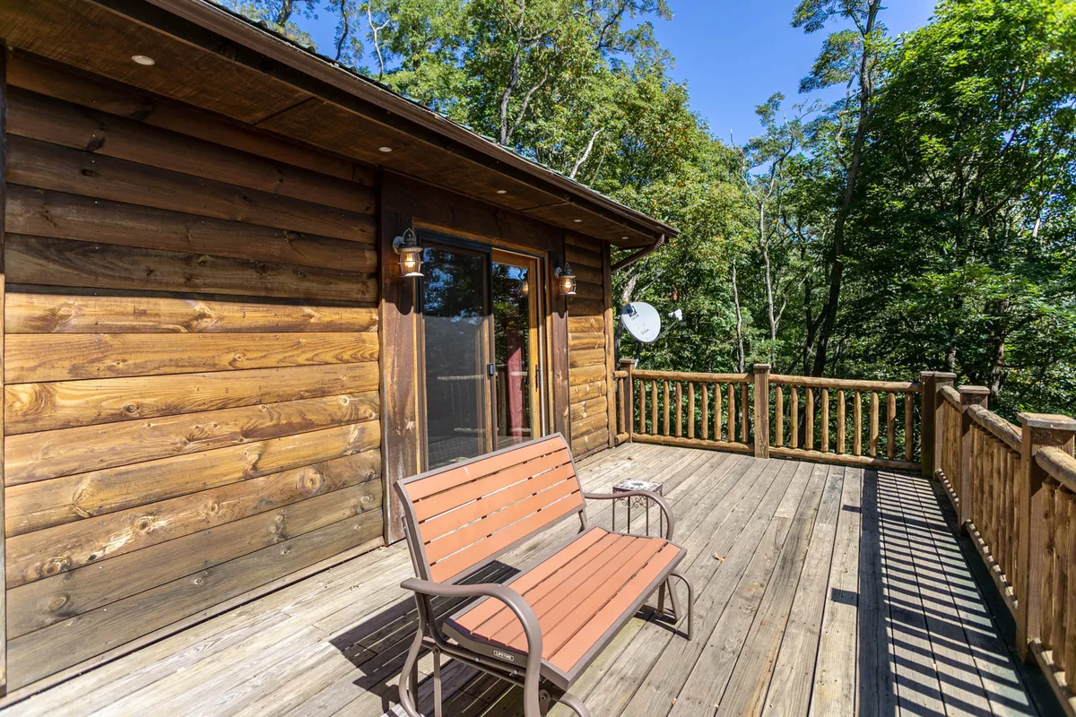 An exterior shot of a wooden deck with a brown bench, glass sliding door, and trees in the background. This deck setting emphasizes the connection to nature, perfect for enjoying the sights and sounds of the forest—and a potential spot for wildlife sightings.