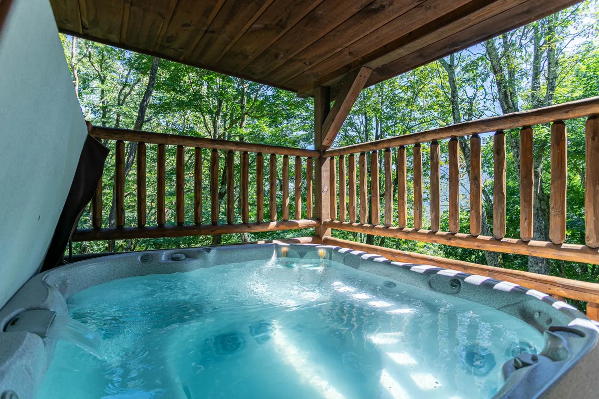 This image showcases a bubbling hot tub set against a wooden railing, surrounded by lush greenery. The setting is tranquil and inviting, emphasizing relaxation and the immersive natural setting. The focus is on the hot tub, with the forest visible through the railings and the sense of privacy and seclusion.
