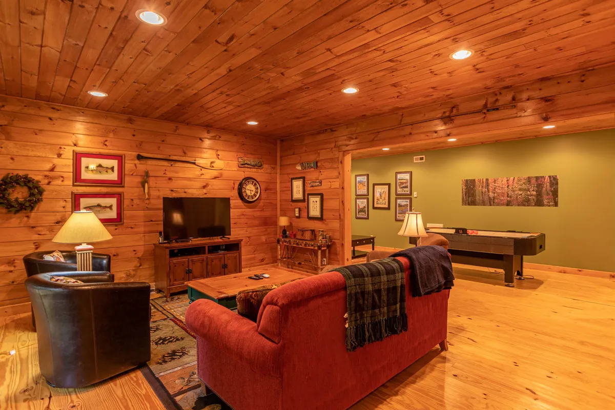 A lower-level living area with a red sofa, black armchair, coffee table, television, and a game table. The space is inviting, perfect for socializing, watching TV, or playing games, and includes the queen sleeper sofa as described.