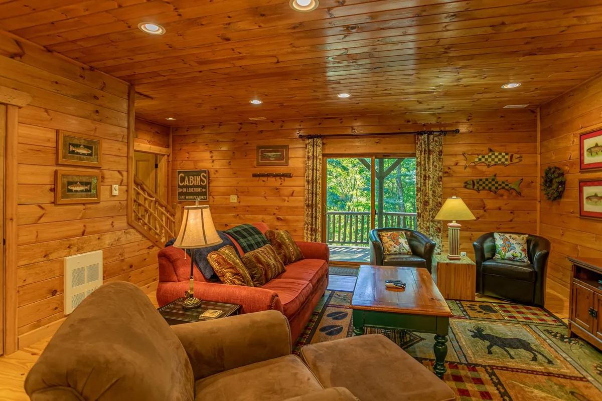 This image features a red sofa positioned next to a large window offering expansive nature views. Decorative lamps and a wooden coffee table add to the inviting ambiance, and the window frames a glimpse of the wooded surroundings outside, hinting at the tranquil, accessible outdoor environment.