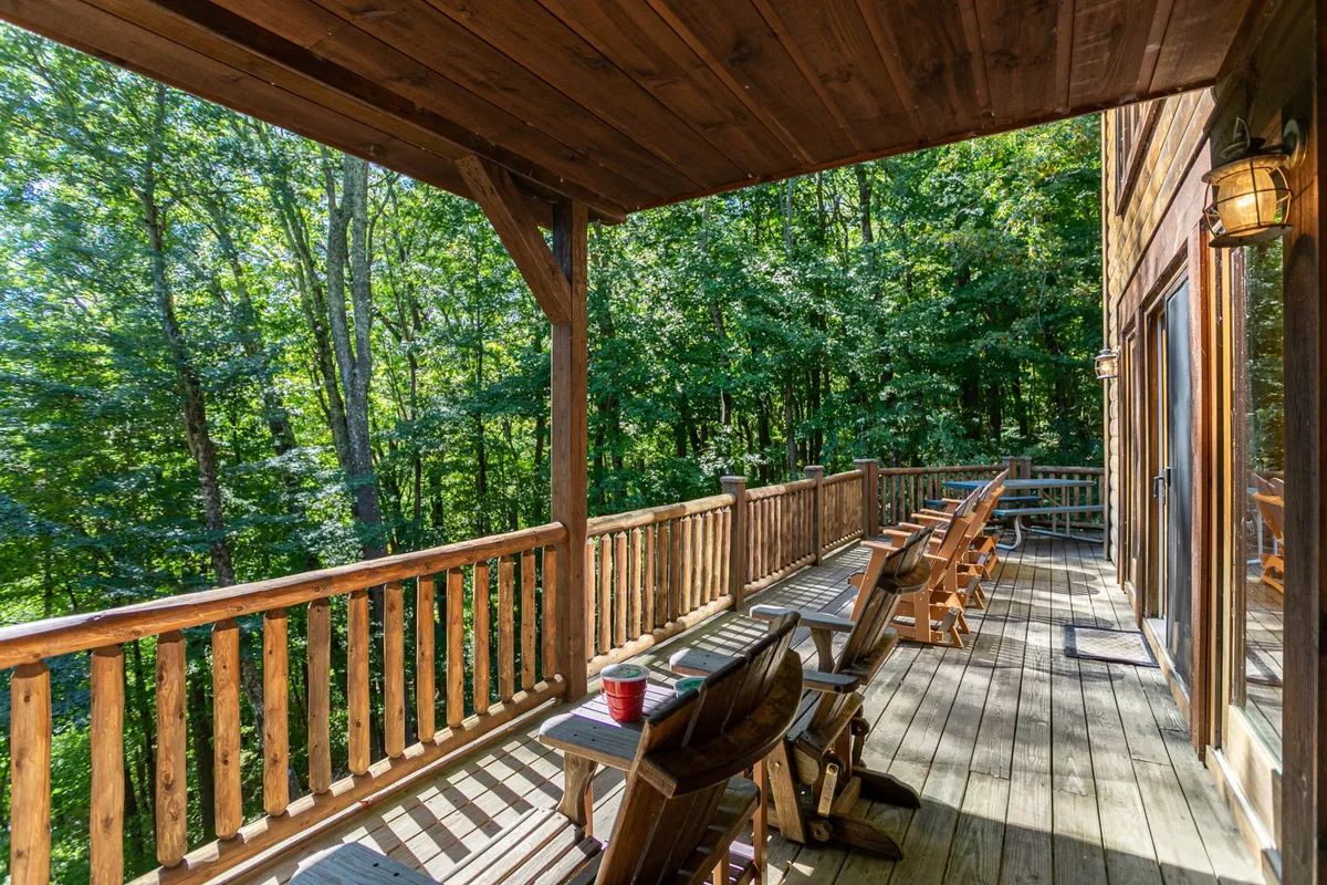 A peaceful deck area with Adirondack chairs and wooden railing, surrounded by mature trees. The setting is serene, inviting guests to lounge, read, or socialize while immersed in the sights and sounds of the forest. The view suggests a private, nature-filled escape.