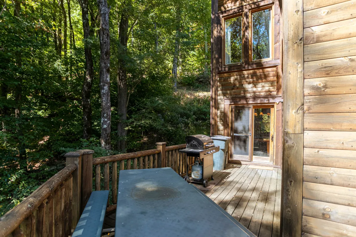 A wooden deck with a gas grill and outdoor dining setup, surrounded by tall trees. The deck offers the perfect setting for al fresco meals, barbecues, or simply relaxing while soaking in the mountain air and scenic views.